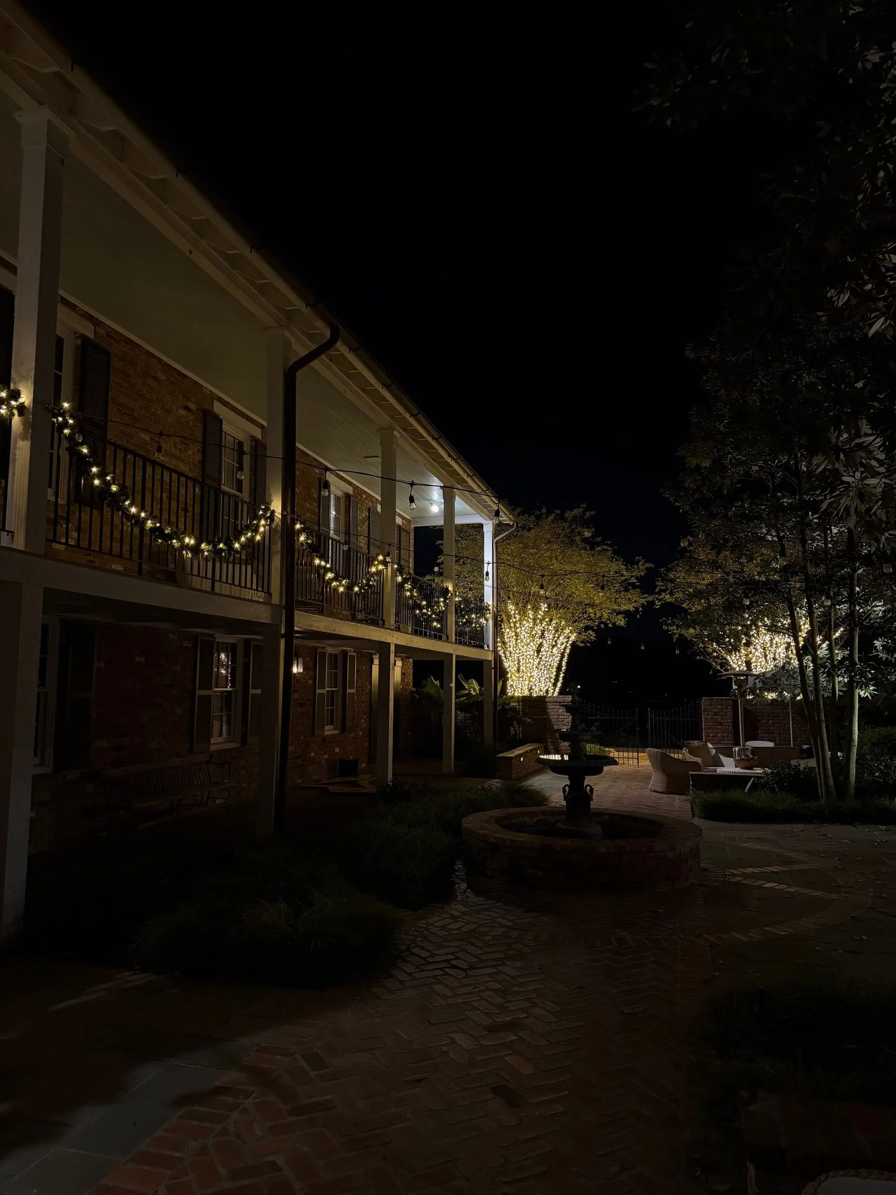 Lit garland on a gallery railing above a courtyard fountain