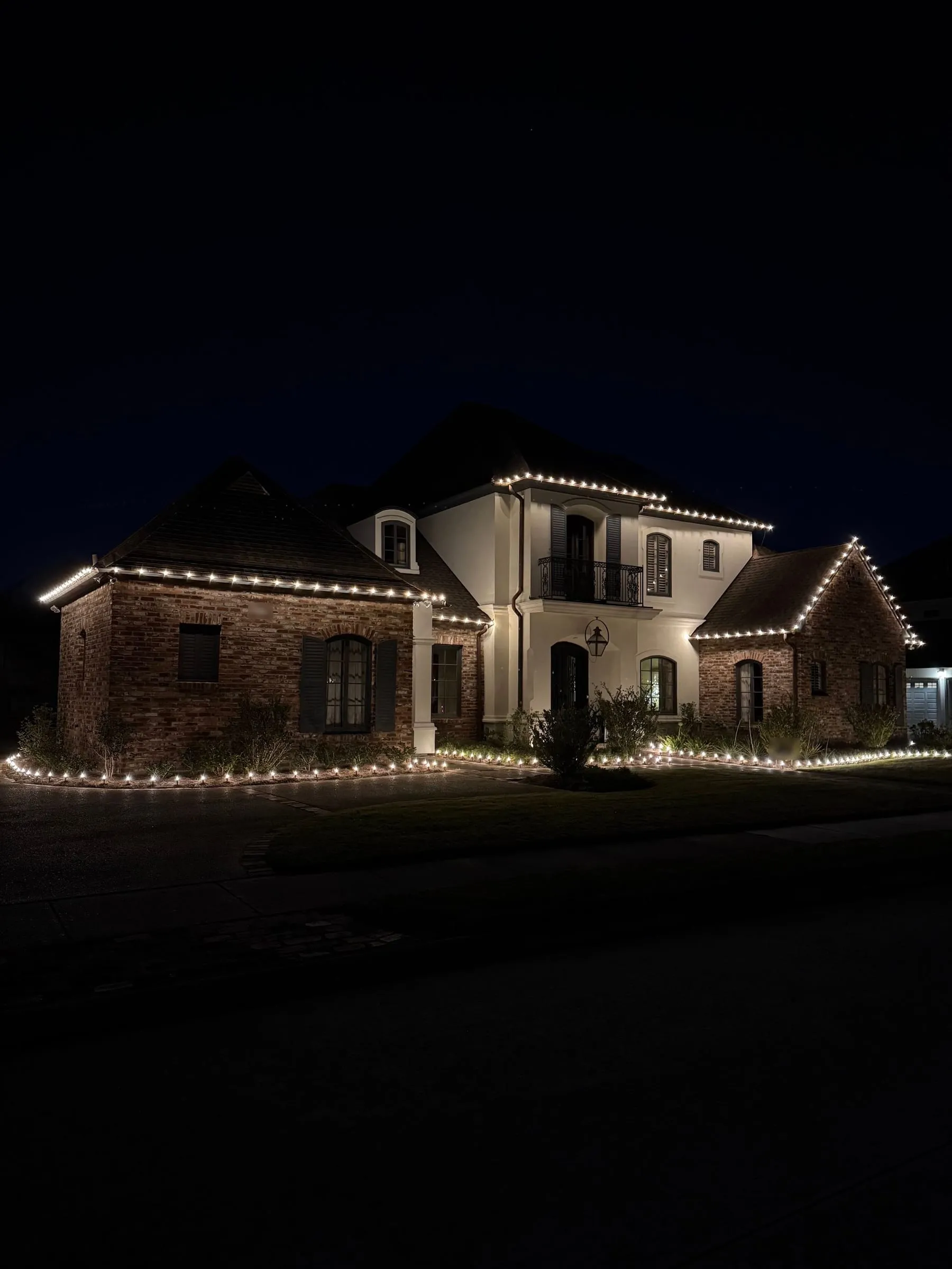 Brick and stucco house with warm white C9 bulbs along the roofline at night